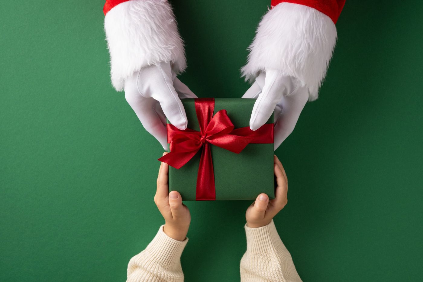 Santa's gloved hands passing a wrapped green gift with a red bow to a child