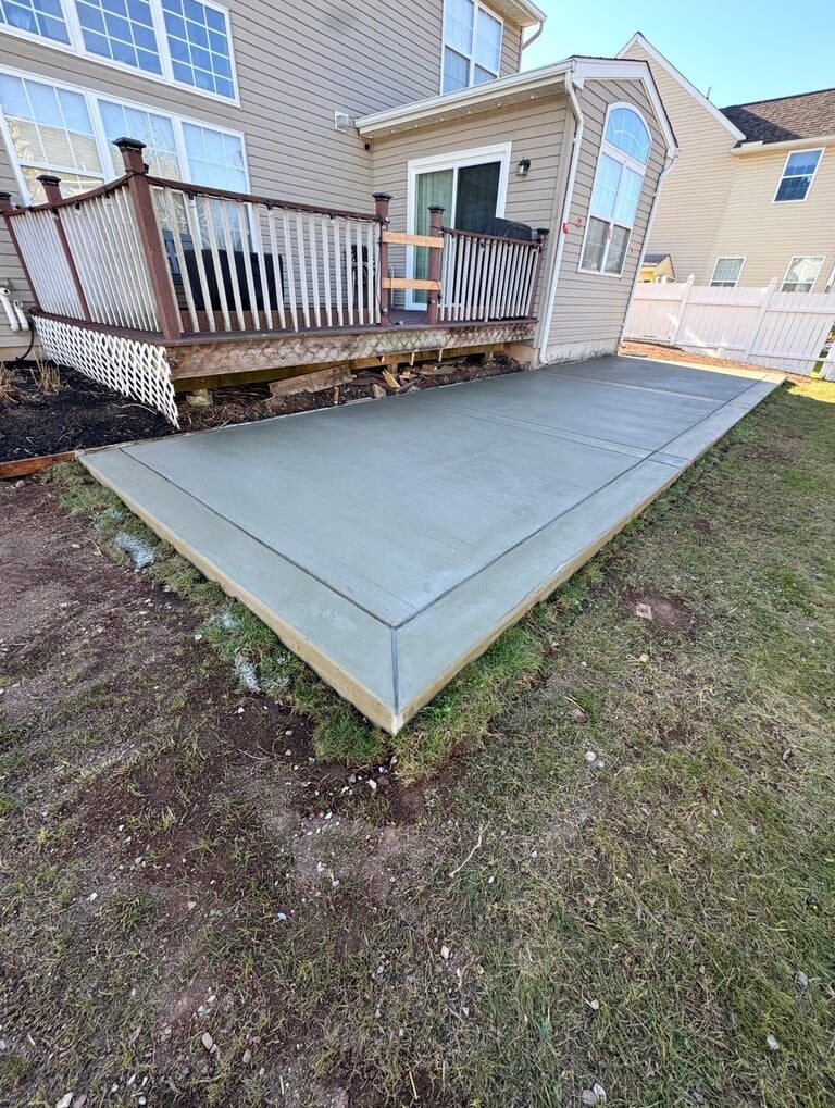 Concrete patio foundation next to residential house with wooden deck and garage door