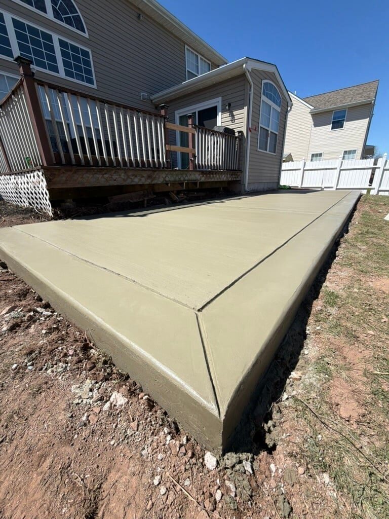 New concrete patio foundation extending from residential home with deck and garage visible