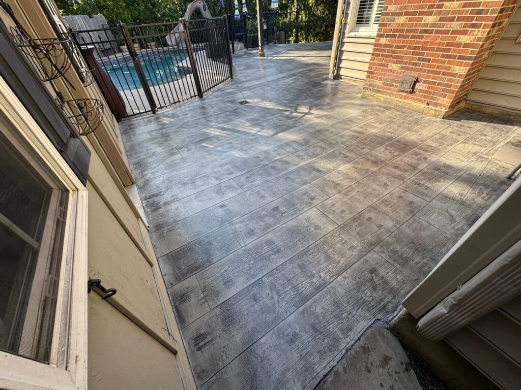 Patio with slate-colored pavers, metal pool fence, brick wall, and trees visible in background