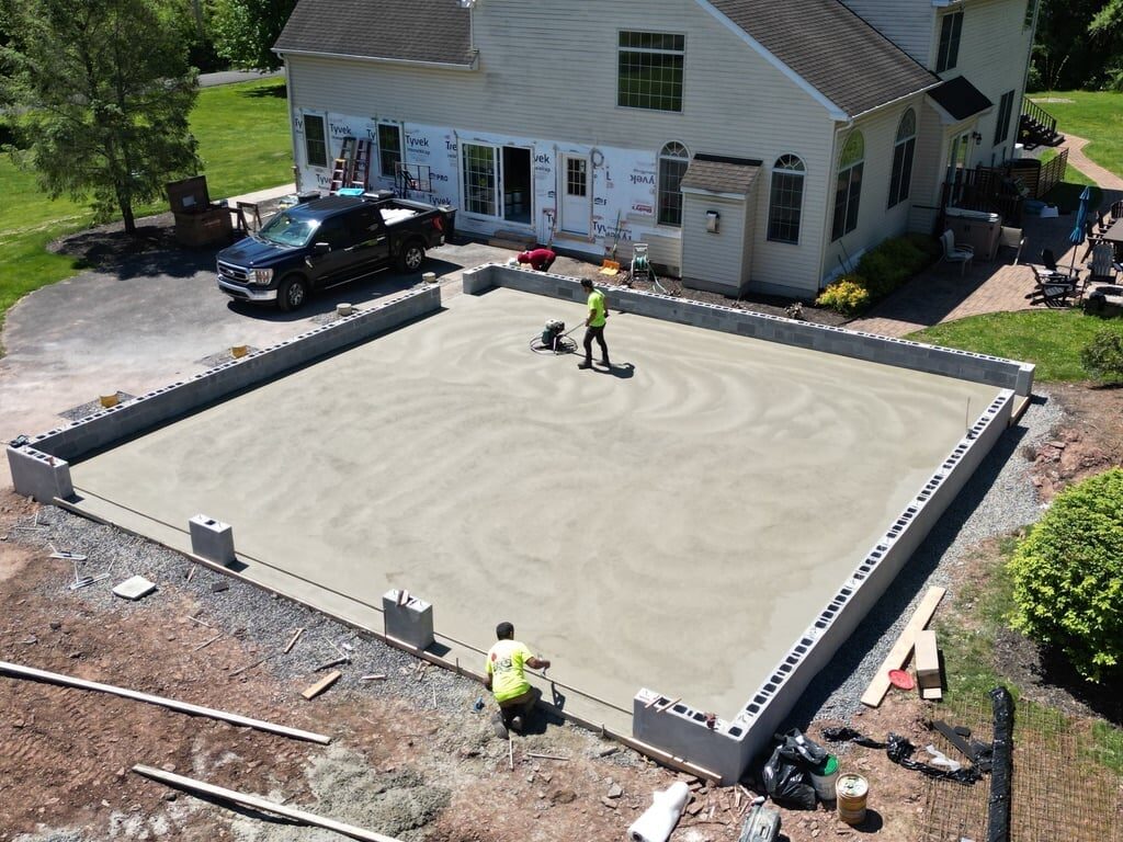 Workers finishing concrete foundation or pad in residential driveway with house and vehicles in background