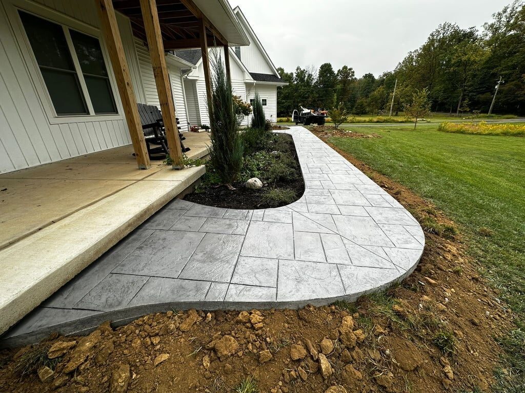Curved paver patio with topiary shrub extending from a modern farmhouse with white exterior, overlooking open green lawn