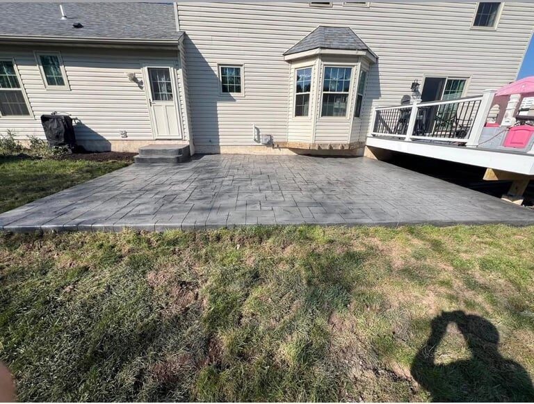 Gray paver patio in backyard of white single-story home with connected sunroom and deck