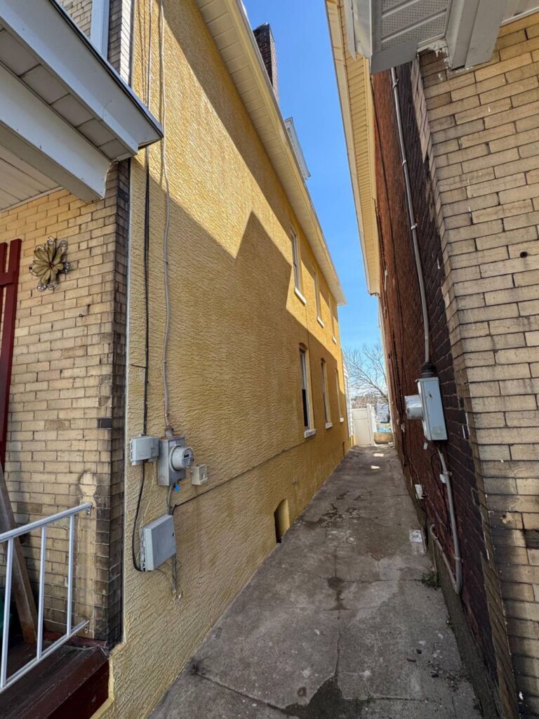Yellow textured stucco side wall between two brick homes