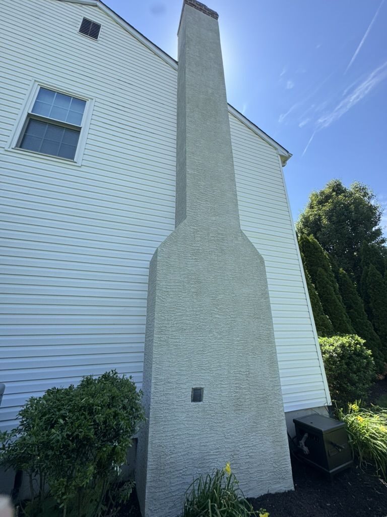 Stucco chimney chase on the side of a vinyl-sided home