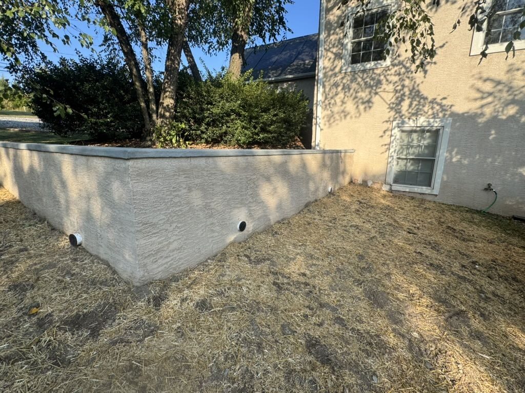 Stucco-finished retaining wall with drain outlets beside a home