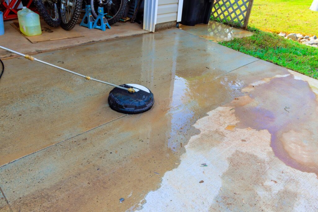 Driveway is being cleaned with high pressure washer, creating shiny surface, removing dirt grime.