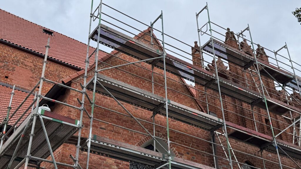 Scaffolding surrounds historic brick building under restoration on a cloudy day showcasing architectural details and renovation work.