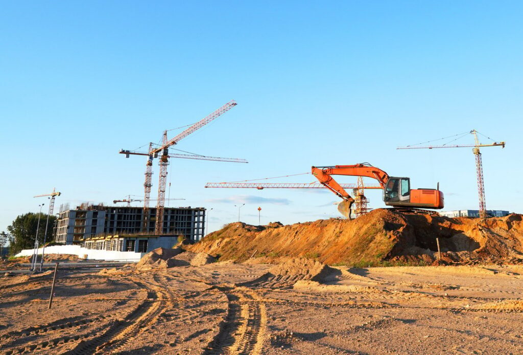 Construction site. Buildings under construction. Tower Cranes on Residential Buildings construction. Excavator on groundwork. Backhoe on roadworks. Excavator on earthworks for road construction.