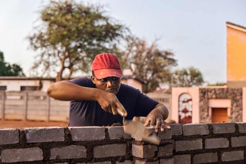 bricklayer african men , using a trowel and align string, building a wall at sunset outdoors
