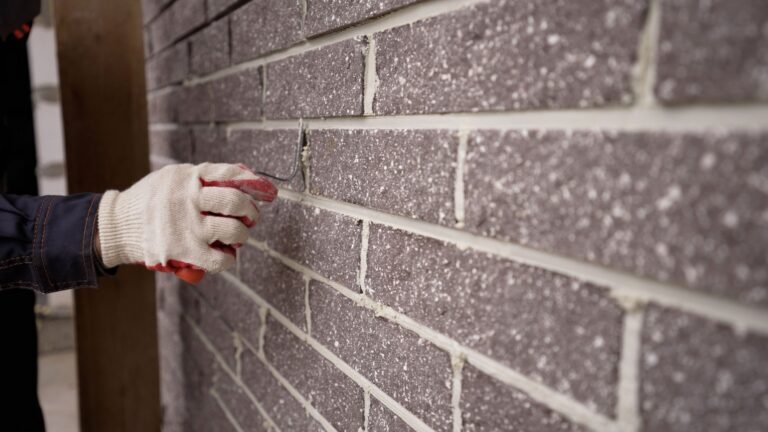 The worker wipes the brickwork of the wall, the bricklayer wipes the seam between the bricks. The builder carefully makes a brick wall, a close-up of a skilled craftsman laying a large masonry of bricks, the concept of a building, builds a house.