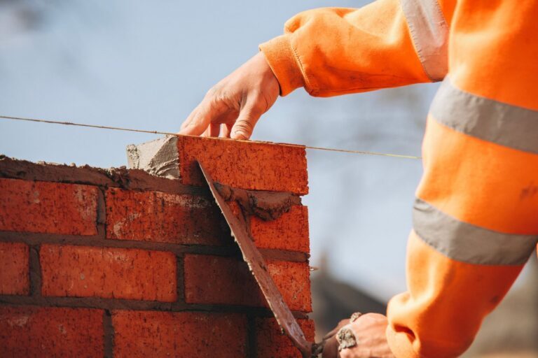 Close-up of skilled bricklayer working on construction site laying one more red brickin the wall