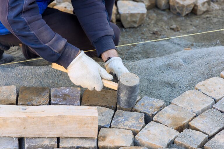 Worker installs stone pavers on prepared surface, carefully aligning each piece with precision.